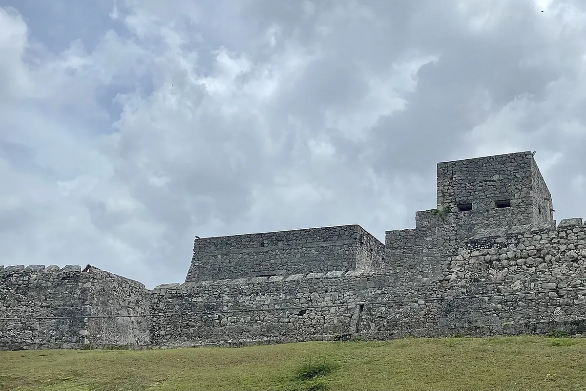 The grey stone walls and corner tower of the Fortress of San Felipe at Bacalar, under a cloudy sky