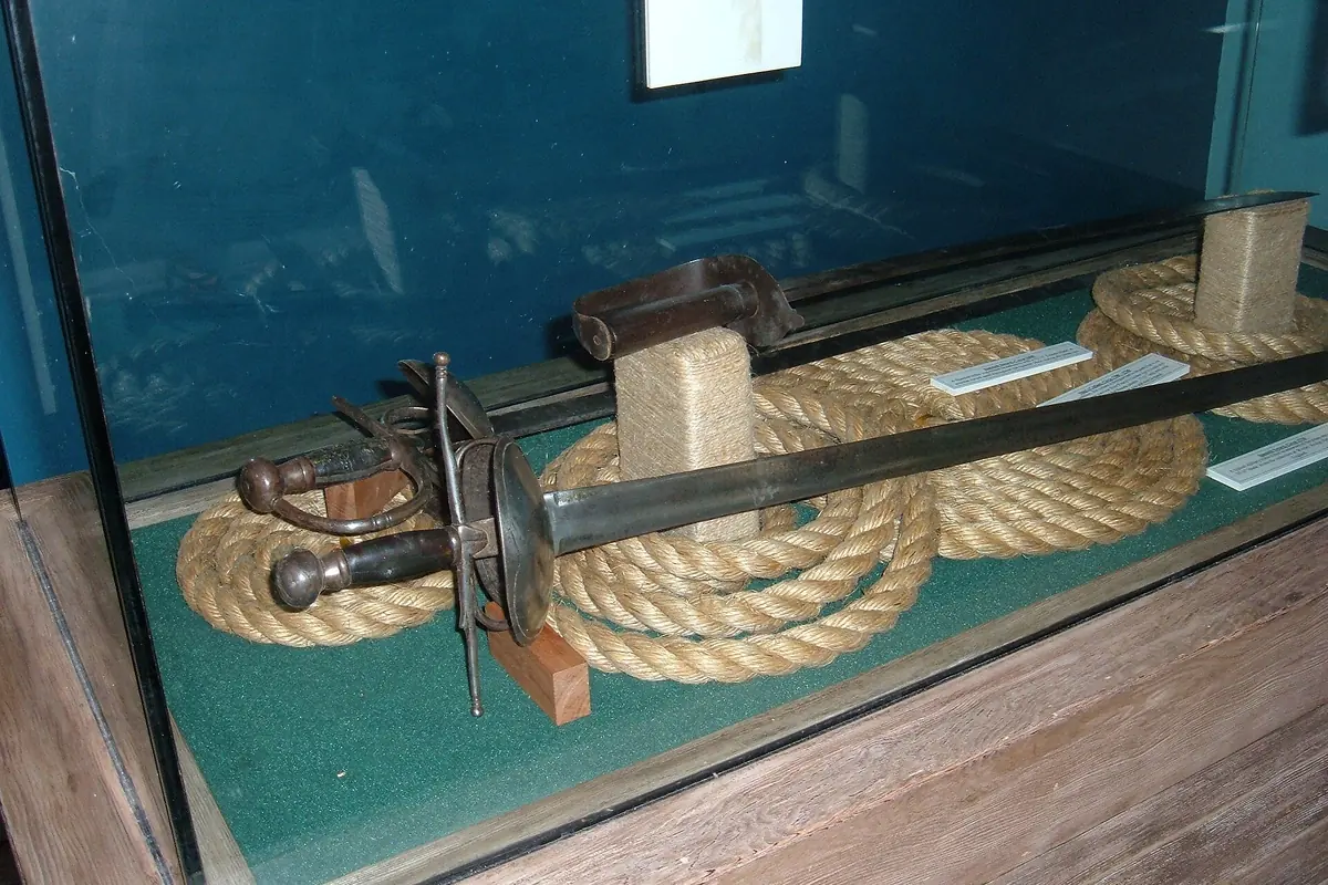 A short sabre with a cupped hilt lying on coiled rope inside a glass museum case