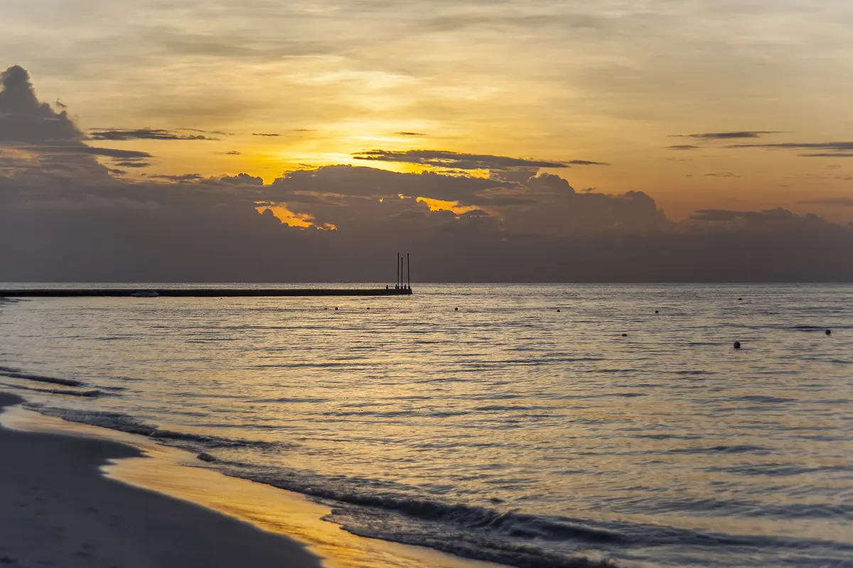 A golden sunset over the Caribbean Sea off Cozumel, with a dark beach in the foreground